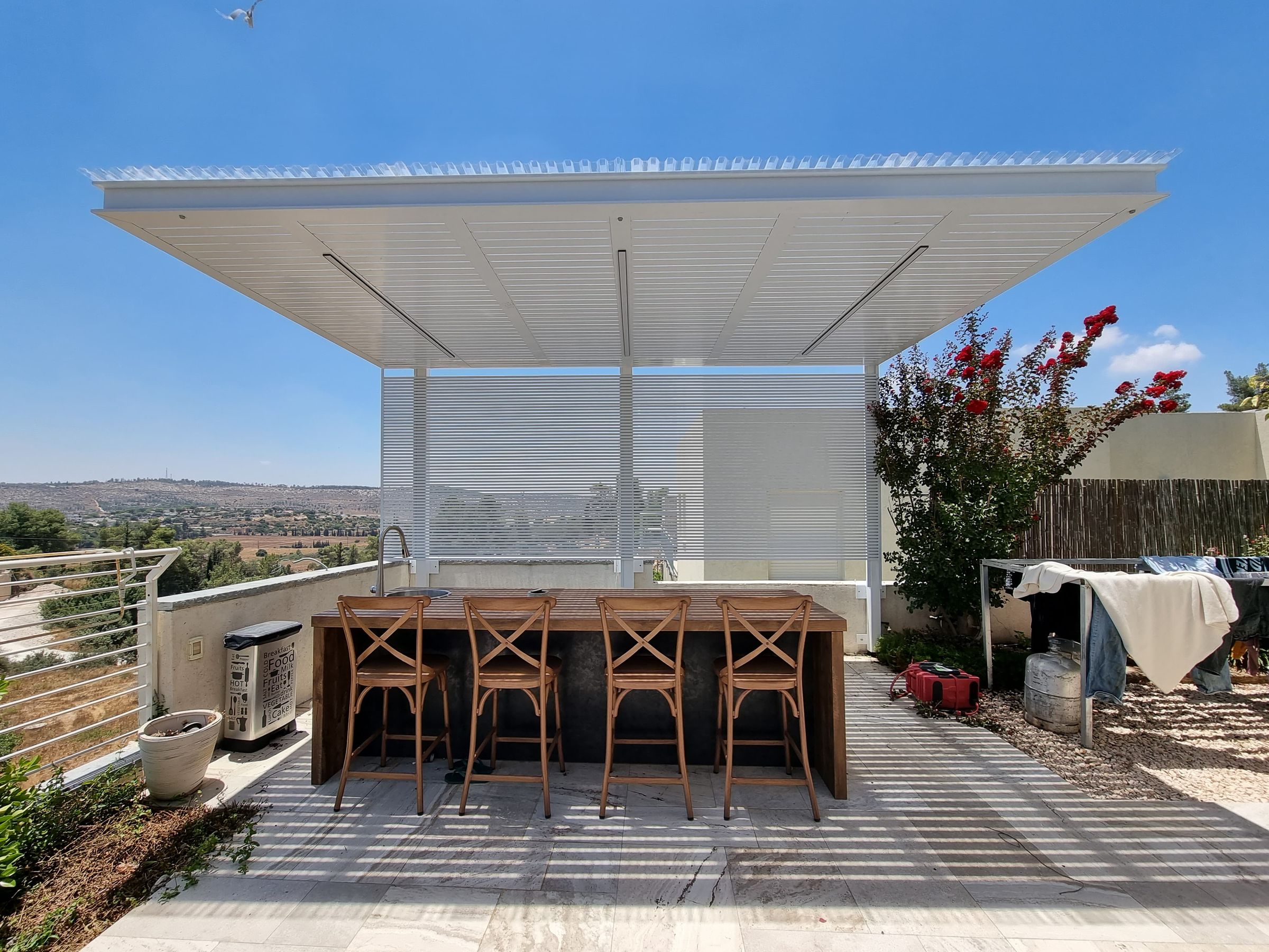 פרגולה לבנה מעל בר חוץ עם כיסאות עץ
